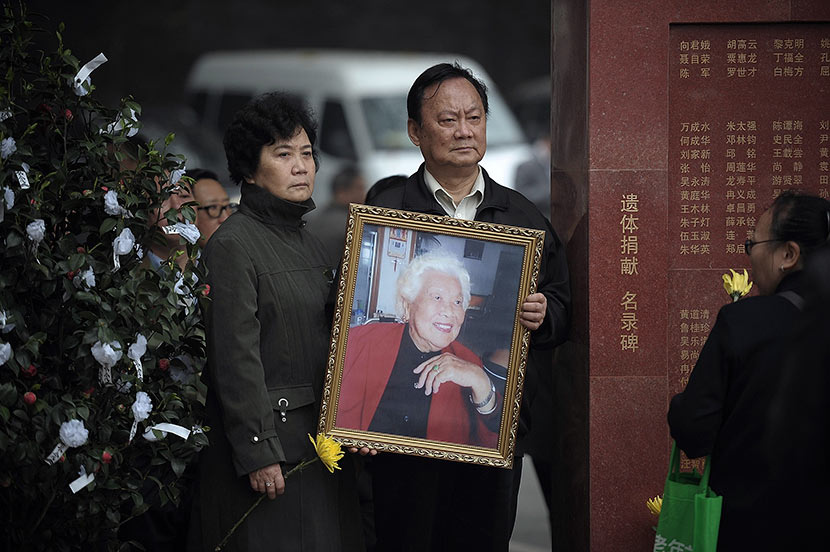 A relative holds a portrait of an organ donor in front of a monument bearing donors’ names at a memorial park in Chongqing, April 4, 2014. Ran Wen/VCG