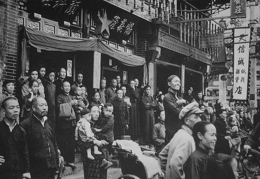 Local people gaze out into the distance from the street in front of a line of shops when PLA soldiers enter the city, in Beijing, spring of 1949. Courtesy of ‘Old Photos’